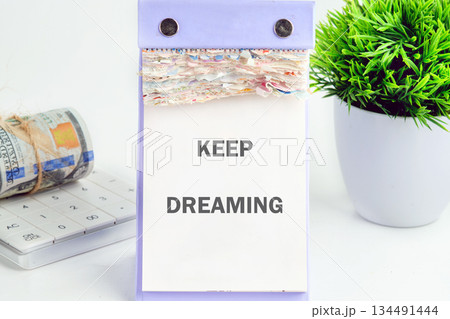 A calendar displays KEEP DREAMING next to money and a plant. It symbolizes aspirations and financial dreams taking root and flourishing in a pristine, optimistic atmosphere 134491444