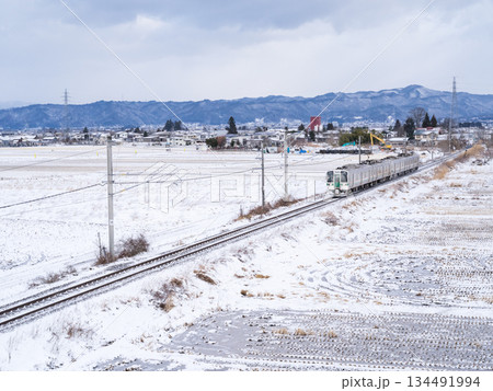 【山形線】冬の田園風景を走行する普通列車 134491994