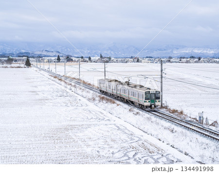 【山形線】冬の田園風景を走行する普通列車 134491998