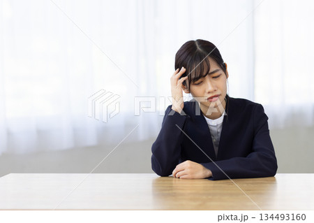 デスクで頭を押さえて悩むスーツ姿の若い女性 デスクで頭を押さえて悩むスーツ姿の若い女性 134493160