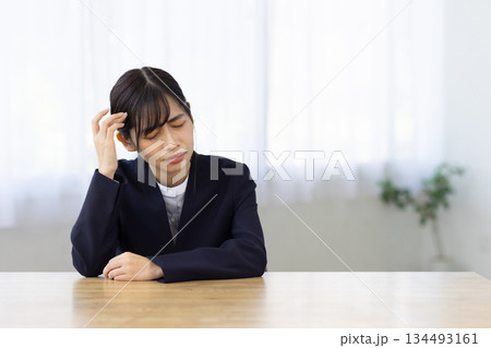 デスクで頭を押さえて悩むスーツ姿の若い女性 134493161