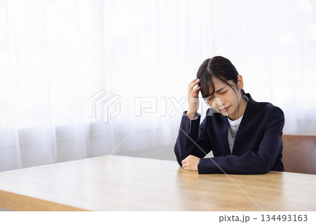 デスクで頭を押さえて悩むスーツ姿の若い女性 デスクで頭を押さえて悩むスーツ姿の若い女性 134493163
