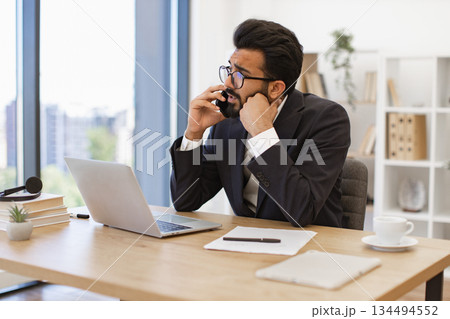 A serious-looking businessman is talking on the phone in his office, looking concerned 134494552