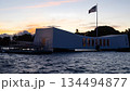 USS Arizona Memorial Pearl Harbor Honolulu Hawaii sunset view with American flag, historic WWII monument silhouette on ocean water, solemn patriotic dusk scene. 134494877