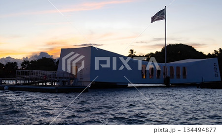 USS Arizona Memorial Pearl Harbor Honolulu Hawaii sunset view with American flag, historic WWII monument silhouette on ocean water, solemn patriotic dusk scene. USS Arizona Memorial Pearl Harbor Honolulu Hawaii sunset view with American flag, historic WWII monument silhouette on ocean water, solemn patriotic dusk scene. 134494877