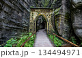 Historic Gothic Gate entrance in Adrspach-Teplice Rocks Czechia with wooden walkway between massive mossy sandstone cliffs in famous Bohemian rock city nature reserve. 134494971