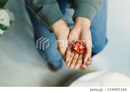 Top view of hand holding small red gift box with gold ribbon 134495184