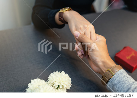 Close up of couple holding hands with red jewelry ring box and flowers 134495187