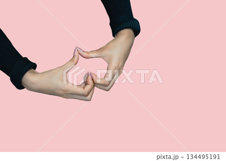 Close up of hands making heart shape on pink background 134495191