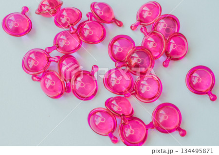 Close-up macro shot of many glossy pink hair treatment capsules. Focused foreground highlights the rich oil and reflective texture 134495871