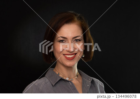 Portrait of a mature woman with an open gaze against a dark background. 134496078