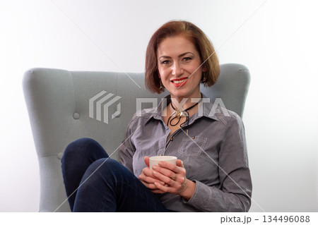 A woman is sitting in a chair and holding a cup in her hands. A woman is sitting in a chair and holding a cup in her hands. 134496088