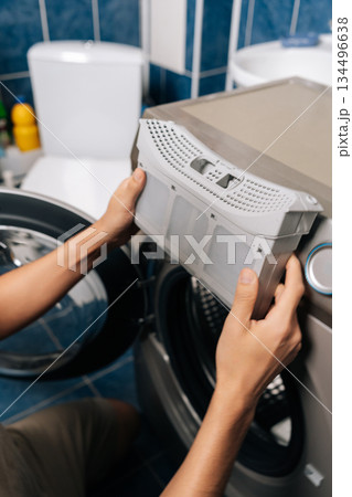 Close-up person removing lint filter from tumble dryer, performing routine appliance maintenance for optimal performance and household safety, preventing fire hazards and improving laundry efficiency. Close-up person removing lint filter from tumble dryer, performing routine appliance maintenance for optimal performance and household safety, preventing fire hazards and improving laundry efficiency. 134496638
