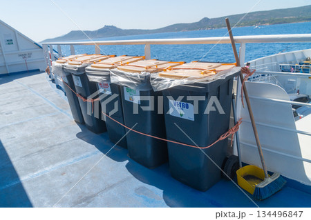 Several secured containers stand on the ferry deck, fastened with ropes for safe transport. The calm sea and distant coastline contrast with the industrial look of the equipment and maritime setting. 134496847