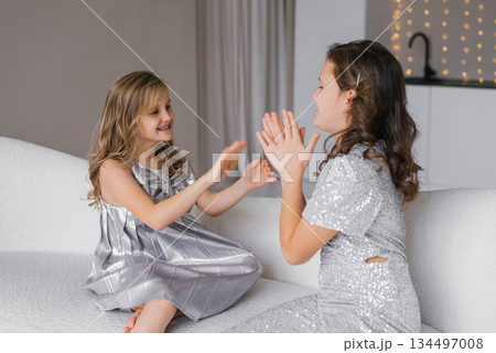 Young girls are playing with each other, wearing a silver dress. They are both smiling and seem to be enjoying their time together 134497008
