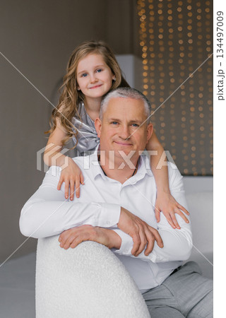 Man and little girl are posing for a picture. Father is wearing white shirt and gray pants, while the daughter is wearing silver dress. Scene is happy and lighthearted 134497009