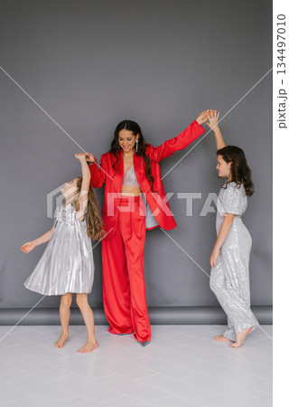 Young woman in red suit is holding the hands of two children. The children are dressed in silver and red. Concept of warmth and family togetherness 134497010