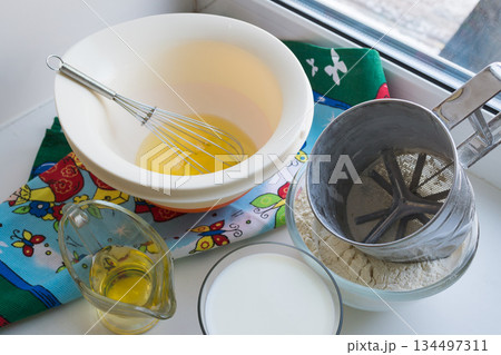 raw ingredients for pancakes are laid out on a multi-colored tablecloth and white background 134497311