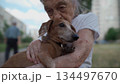 Animal theme is a lonely old woman best friend. Caucasian 90 years old senior female is happy to spend time with her pet small dachshund dog, holding her in her arms, hugging hugs and kisses outdoor 134497670