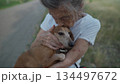 Senior 90-year-old woman with gray hair and deep wrinkles sits outdoors In assisted living facility on bench with small dachshund dog. Old female hugs and cuddles pet in the park on a bench 134497672