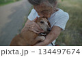 Happy senior woman holds a small dachshund dog in her arms, smiles hugs, presses and shows love to her pet on a bench in the park. Female 90 years old spends time with her best friend pet on street 134497674