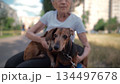 Animal theme is a lonely old woman best friend. Caucasian 90 years old senior female is happy to spend time with her pet small dachshund dog, holding her in her arms, hugging hugs and kisses outdoor 134497678