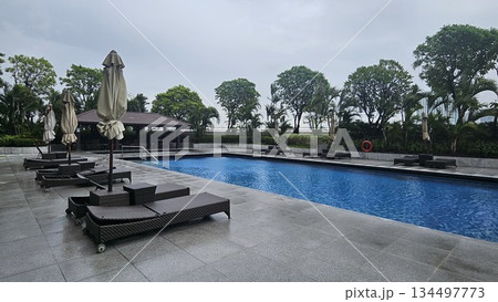 A serene poolside with wicker loungers, closed umbrellas A serene poolside with wicker loungers, closed umbrellas 134497773
