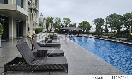 A serene poolside with wicker loungers, closed umbrellas A serene poolside with wicker loungers, closed umbrellas 134497786