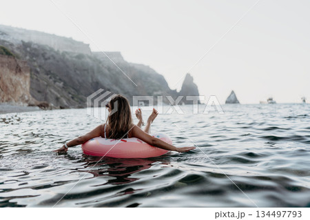Woman, floating, ocean, relaxing on an inflatable ring near coastal cliffs with copy space. Woman, floating, ocean, relaxing on an inflatable ring near coastal cliffs with copy space. 134497793