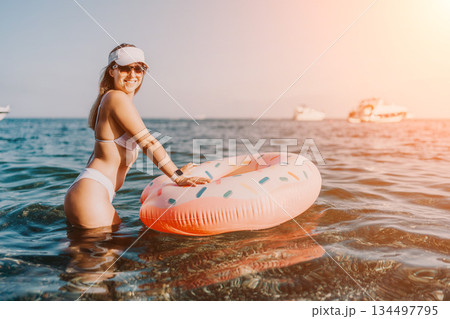 Woman, beach, vacation. Woman in bikini stands in ocean water with donut ring, enjoying summer vacation. 134497795