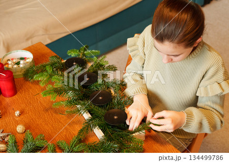 Child arranging advent wreath with candles and pine branches Child arranging advent wreath with candles and pine branches 134499786
