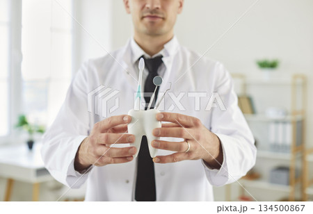 Doctor dentist holding toy tooth with dental tools and toothbrush standing in dentistry clinic. Doctor dentist holding toy tooth with dental tools and toothbrush standing in dentistry clinic. 134500867