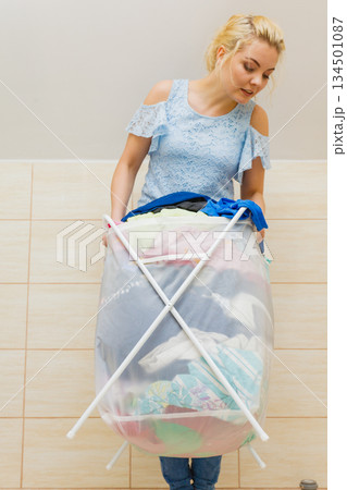 Woman carry big basket of dirty clothes laundry. 134501087