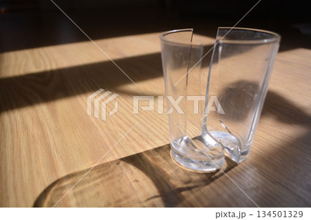 A top view of a child's hands holding two broken pieces of a clear glass on a wooden surface. Conceptual concepts: safety, household accidents, child safety, parental control. A top view of a child's hands holding two broken pieces of a clear glass on a wooden surface. Conceptual concepts: safety, household accidents, child safety, parental control. 134501329