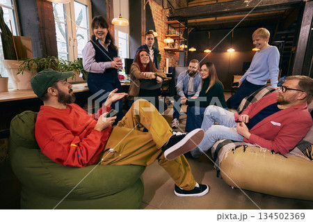 Group of coworkers relaxing and talking in modern workspace. 134502369