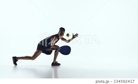 Female padel player moving forward and reaching ball in studio. 134502417