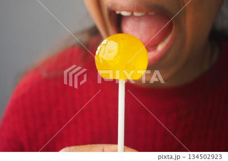Person holds yellow lollipop before mouth in indoor setting Person holds yellow lollipop before mouth in indoor setting 134502923