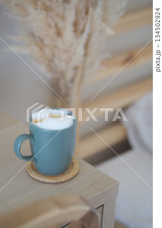 Coffee cup sits on table beside plant in a home setting Coffee cup sits on table beside plant in a home setting 134502924