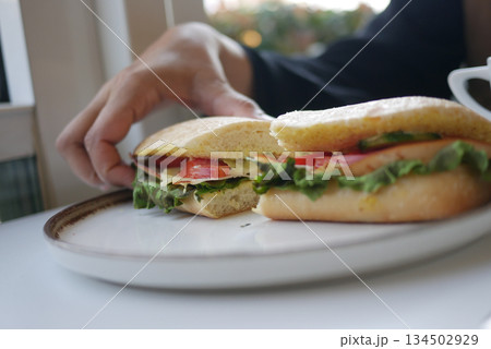 A hand reaches for a sandwich on a plate with vegetables inside A hand reaches for a sandwich on a plate with vegetables inside 134502929