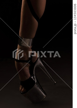 Dancer wears high heel platform shoes with ankle strap in dark studio during dance performance 134503806