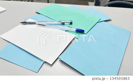 A white table with colored sheets of paper and a pen, suitable for creative brainstorming, note-taking concepts, and minimalist stationery photography. 134503863
