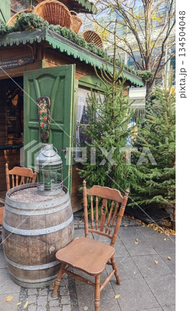 Rustic outdoor market stall with wooden furniture, barrel table, lantern, and small fir trees creating a traditional atmosphere. The image represents cozy Christmas market, nostalgia 134504048