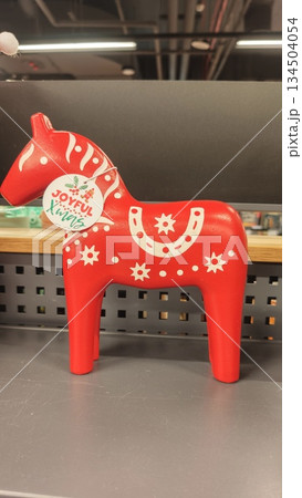 Red wooden Dala horse figurine with white folk patterns displayed on a shop counter. The image represents Scandinavian tradition, handmade craft, and festive Christmas decor concept Red wooden Dala horse figurine with white folk patterns displayed on a shop counter. The image represents Scandinavian tradition, handmade craft, and festive Christmas decor concept 134504054