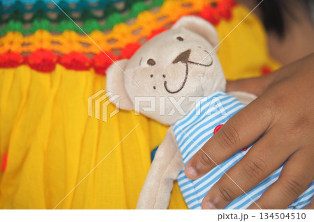 Child holds teddy bear in colorful dress 134504510