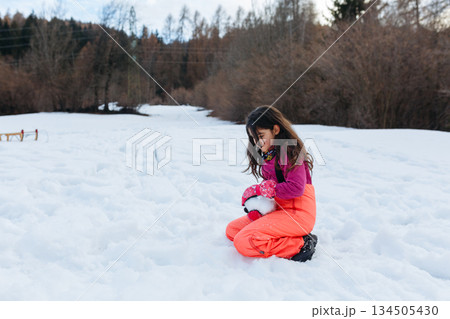 one girl sitting on the snow and making snow ball 134505430