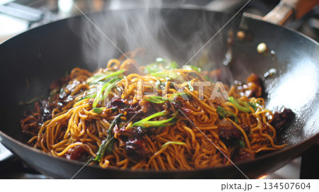hot stir-fried noodles glistening with dark sauce, mixed with meat and fresh green onions inside large, dark wok. Steam rises dramatically from authentic Chinese or Asian dish being cooked on stove 134507604