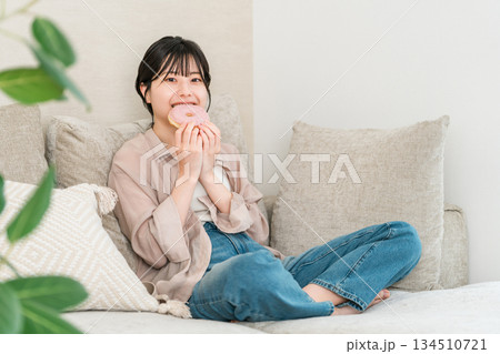 リビングのソファーに座りドーナツを食べる若いアジア人女性 134510721