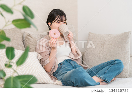 リビングのソファーに座りドーナツを食べる若いアジア人女性 134510725
