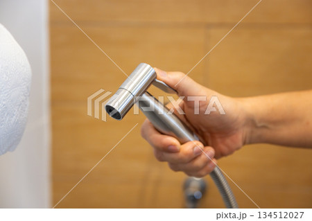 Woman is holding a stainless steel handheld bidet sprayer in bathroom. Woman is holding a stainless steel handheld bidet sprayer in bathroom. 134512027