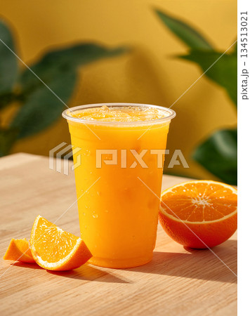 Iced Fresh Orange Juice in Plastic Takeaway Cup on Wooden Table with Sliced Citrus, Bright Natural Sunlight and Green Leaves Background, Healthy Summer Refreshment Concept for Cafe Menu. Iced Fresh Orange Juice in Plastic Takeaway Cup on Wooden Table with Sliced Citrus, Bright Natural Sunlight and Green Leaves Background, Healthy Summer Refreshment Concept for Cafe Menu. 134513021